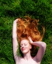 Portrait of a beautiful young sexy red-haired woman, lying in the spring sun in happiness, relaxing on the green grass, the red Royalty Free Stock Photo