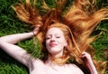 Portrait of a beautiful young sexy red-haired woman spreading hair fan-shaped, with relaxed shoulders lying on the grass and Royalty Free Stock Photo