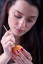 Portrait of a beautiful young sexy woman paints an orange Easter egg according to Sorbian tradition with a needle head and melted