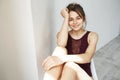 Portrait of beautiful young tender girl in vinous swimwear smiling looking at camera posing on chair over white wall.