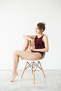 Portrait of beautiful young tender model in burgundy swimwear smiling posing sitting in chair over white wall. Royalty Free Stock Photo