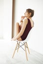 Portrait of beautiful young tender model in burgundy swimwear smiling posing sitting in chair over white wall. Royalty Free Stock Photo