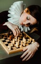 Portrait of an young woman in an antique dress with a white frill, who is thinking about the next move in a chess game. The queen Royalty Free Stock Photo