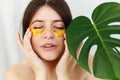 Portrait of beautiful young woman applying golden eye patches on fresh soft skin at green palm leaf on white background. Happy Royalty Free Stock Photo