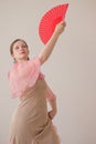 Portrait of a beautiful young woman in a beige and pink dress on a beige background. She is dancing flamenco. A hand with a red