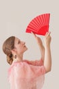 Portrait of a beautiful young woman in a beige and pink dress on a beige background. She is dancing flamenco. Hands with a red fan Royalty Free Stock Photo