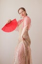 Portrait of a beautiful young woman in a beige and pink dress on a beige background. She is dancing flamenco with a red fan Royalty Free Stock Photo