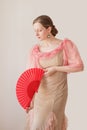 Portrait of a beautiful young woman in a beige and pink dress on a beige background. She is dancing flamenco with a red fan Royalty Free Stock Photo