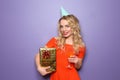 Portrait of beautiful young woman with birthday gift and glass of champagne on color background Royalty Free Stock Photo