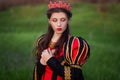 Portrait of a beautiful, young woman in a black and red medieval dress with a crown on her head. Princess walk in the green field. Royalty Free Stock Photo