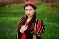 Portrait of a beautiful, young woman in a black and red medieval dress with a crown on her head. Princess walk in the green field. Royalty Free Stock Photo