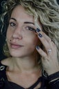 Portrait of a beautiful young woman with blond curly hair who fixes her eye makeup with her finger Royalty Free Stock Photo