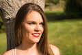 Portrait of beautiful young woman, blonde, blue eyes, leaning against a tree trunk in an outdoor park on a sunny day. Concept Royalty Free Stock Photo