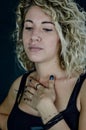 Portrait of a beautiful young woman with blonde curly hair with her hand on her chest looking down with consternation