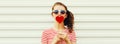 Portrait of beautiful young woman blowing her lips with lipstick with red sweet heart shaped lollipop on white background Royalty Free Stock Photo