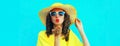 Portrait of beautiful young woman blowing her lips sending sweet air kiss posing wearing yellow summer straw hat, dress on blue Royalty Free Stock Photo