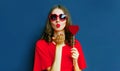 portrait beautiful young woman blowing red lips sending sweet air kiss with red heart shaped lollipop wearing sunglasses on blue Royalty Free Stock Photo