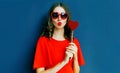 Portrait beautiful young woman blowing red lips sending sweet air kiss with red heart shaped lollipop wearing sunglasses Royalty Free Stock Photo