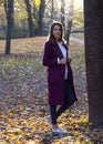 Portrait of beautiful young woman in blue jeans, white shirt and purple coat in autumn park. Royalty Free Stock Photo