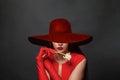 Portrait of a beautiful young woman brunette in red dress and red wide broad brim hat on black