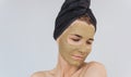 Portrait of beautiful young woman with clay face mask doing wellness therapy, posing against white studio wall. Horizontal shot of Royalty Free Stock Photo