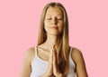 Young woman with closed eyes and hands in praying gesture. Meditation, balance and peace of mind concept. Isolated over pink Royalty Free Stock Photo