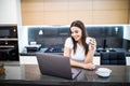 Portrait of a beautiful young woman with coffee cup using laptop in the kitchen at home Royalty Free Stock Photo