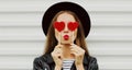 Beautiful young woman covering her eyes with red heart shaped lollipop blowing red lips sending sweet air kiss on a Royalty Free Stock Photo