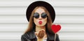 beautiful young woman covering her eyes with red heart shaped lollipop blowing red lips sending sweet air kiss on a Royalty Free Stock Photo