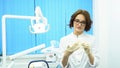 Portrait of a beautiful, young woman doctor wearing medical gloves. Female dental assistant in glasses putting on gloves