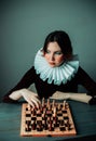 Portrait of a beautiful young woman in a dress with a white frill, who is playing chess. A difficult game. A game of chess