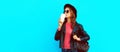 Portrait of beautiful young woman drinking coffee wearing black round hat, black jacket on blue background Royalty Free Stock Photo