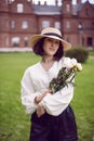 portrait of a beautiful young woman in a hat and a white blouse standing on a green meadow in summer and holding a Royalty Free Stock Photo