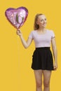 Portrait of beautiful young woman holding heart shaped birthday balloon over yellow background Royalty Free Stock Photo