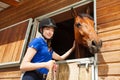 Happy jockey girl stroking horse at riding stable