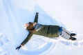 Portrait of a beautiful young woman laying down on a frozen snow lake moving her arms and legs up and down creating a snow angel
