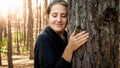 Portrait of beautiful young woman leaning and touching big old tree in forest. Concept of ecology, environment Royalty Free Stock Photo