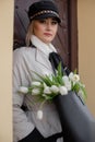 Portrait of beautiful young woman in light coat, standing on street, holding bag with bouquet of tulips. Flower gifts. Royalty Free Stock Photo