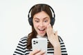 Portrait of beautiful young woman listens to music in wireless headphones, uses her mobile phone, smiles and looks happy Royalty Free Stock Photo