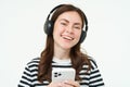 Portrait of beautiful young woman listens to music in wireless headphones, uses her mobile phone, smiles and looks happy Royalty Free Stock Photo