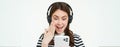 Portrait of beautiful young woman listens to music in wireless headphones, uses her mobile phone, smiles and looks happy Royalty Free Stock Photo