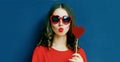 Portrait of beautiful young woman with lollipop blowing red lips sending sweet air kiss wearing a red heart shaped sunglasses Royalty Free Stock Photo