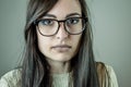 Portrait of a beautiful young woman with long brown hair and eyeglasses looking seriously