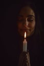 Portrait of a beautiful young woman with long hair holding a lit candle in her hand and praying with closed eyes Royalty Free Stock Photo