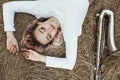 Portrait of a beautiful young woman lying on the dry grass next to the saxophone, face of blonde girl on the hay rests with a Royalty Free Stock Photo