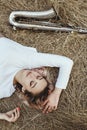 Portrait of a beautiful young woman lying on the dry grass next to the saxophone, face of blonde girl on the hay rests with a Royalty Free Stock Photo