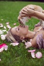 portrait of a beautiful young woman lying on a green meadow with rose petals and holding a rabbit in her hands in front Royalty Free Stock Photo