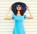 Portrait beautiful young woman model posing wearing blue dress, summer round straw hat on city street over white wall Royalty Free Stock Photo