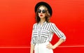 Portrait beautiful young woman model wearing white striped shirt, black round hat posing over red wall Royalty Free Stock Photo