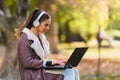 Portrait of beautiful young woman in the park using laptop computer listening over headphones studying outdoors in the nature Royalty Free Stock Photo